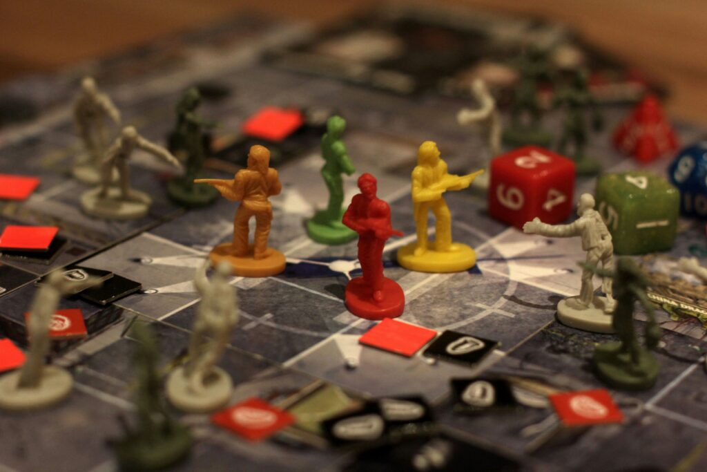 Board game scene with colorful plastic figures and dice on a grid. Figures in red, yellow, and green suggest strategy and tension in gameplay.